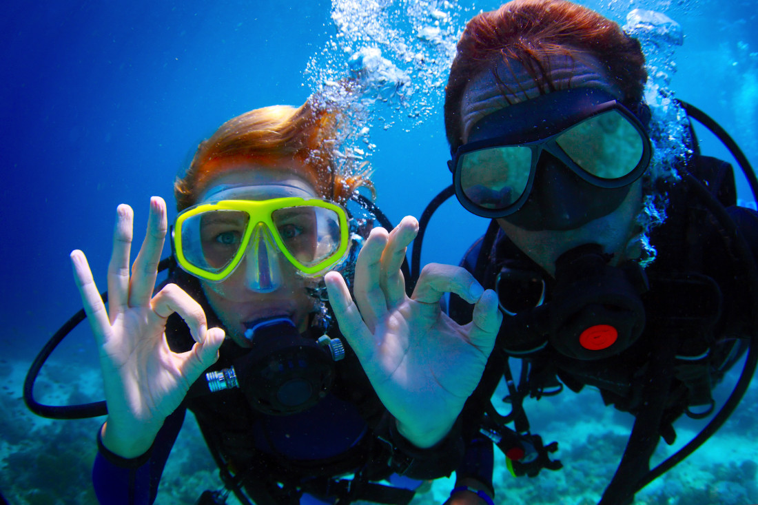 Underwater shoot of a couple diving with scuba and showing ok signal